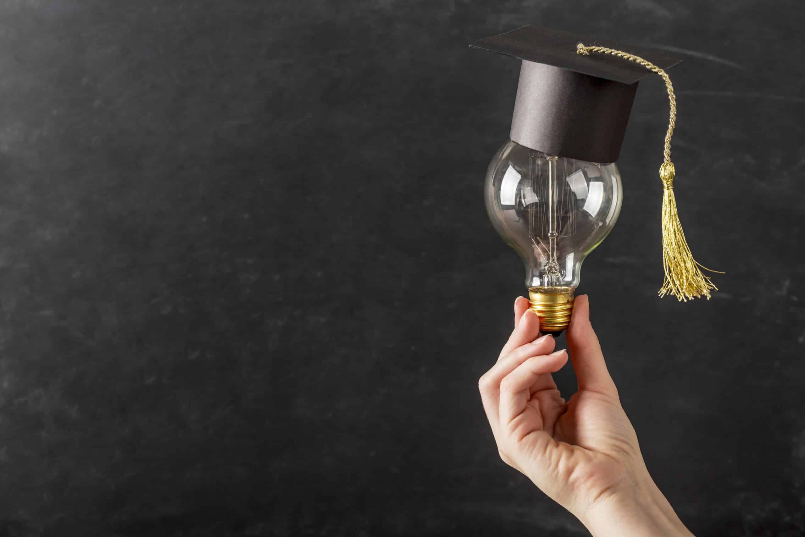 person holding light bulb with graduation cap scaled